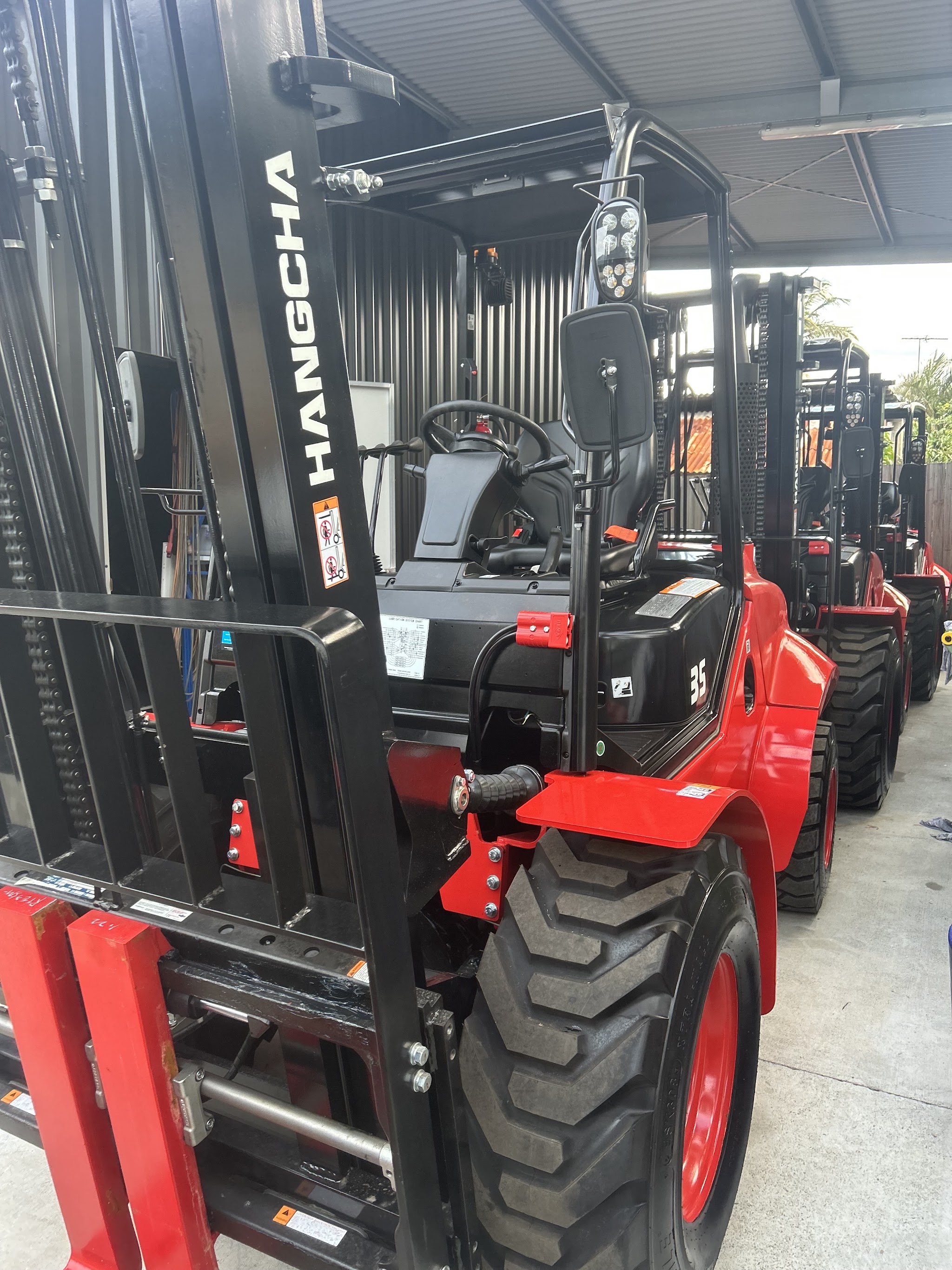 A row of new rough terrain forklifts parked under the workshop awning